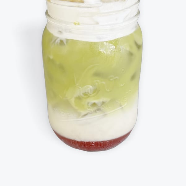 Mason jar with layered green matcha, white cream, and red fruit puree.