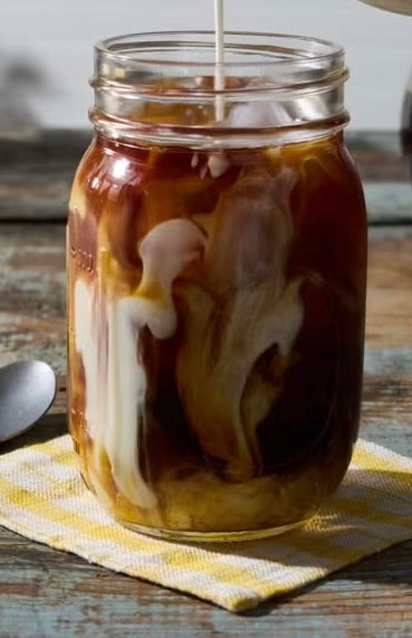 Cream pouring into a mason jar of iced coffee, creating swirling patterns.