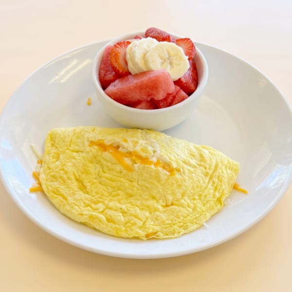 Cheese omelet and a fruit salad with strawberries, watermelon, and bananas on a white plate.