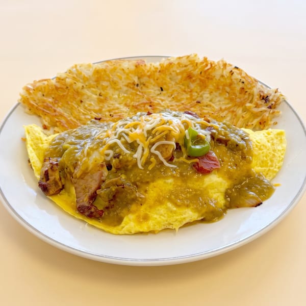 Savory omelet topped with green chili sauce and shredded cheese, served with crispy hash browns.