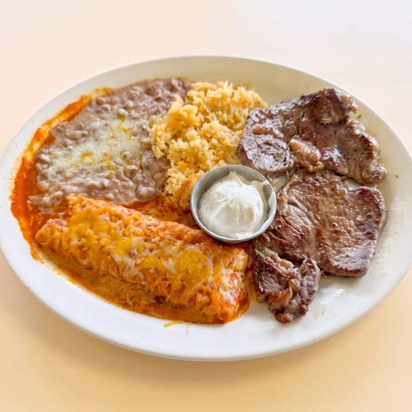 Mexican combo plate with grilled steak, cheesy enchilada, refried beans, rice, and sour cream.