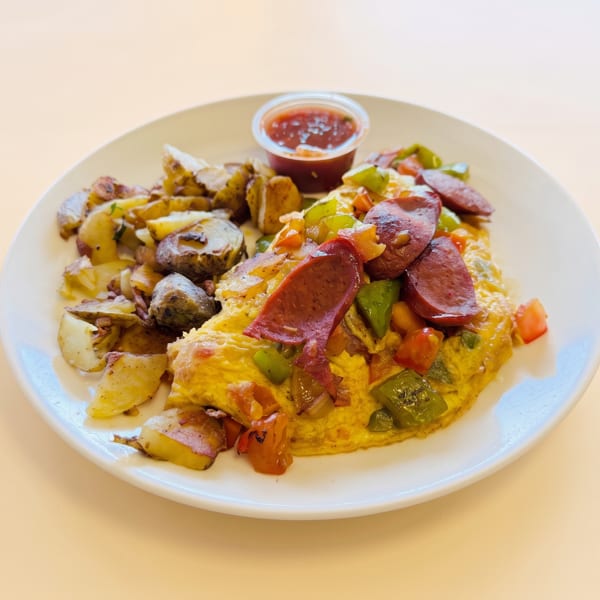 A breakfast plate with an omelet topped with sausage and peppers, alongside roasted potatoes and salsa.
