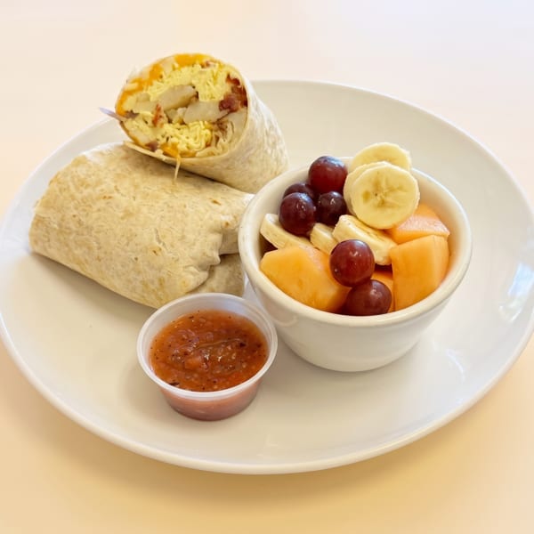 Delicious breakfast burrito with a side of fresh fruit and salsa on a white plate.