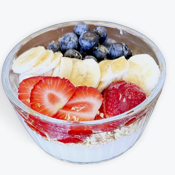 Glass bowl of yogurt and oats topped with fresh blueberries, sliced bananas, strawberries, and goji berries.